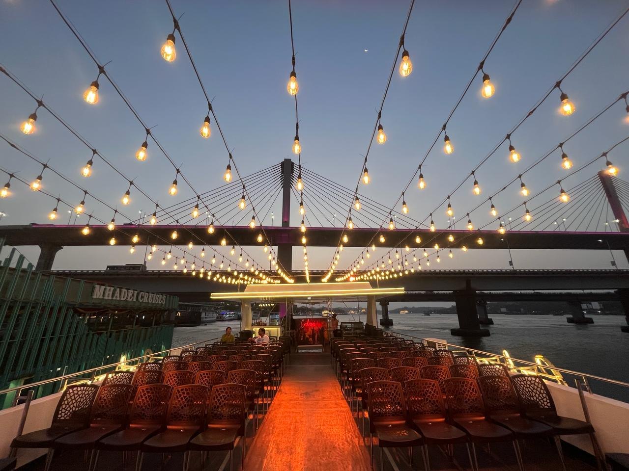 Calma Cruise open deck at dusk with string lights on the Mandovi